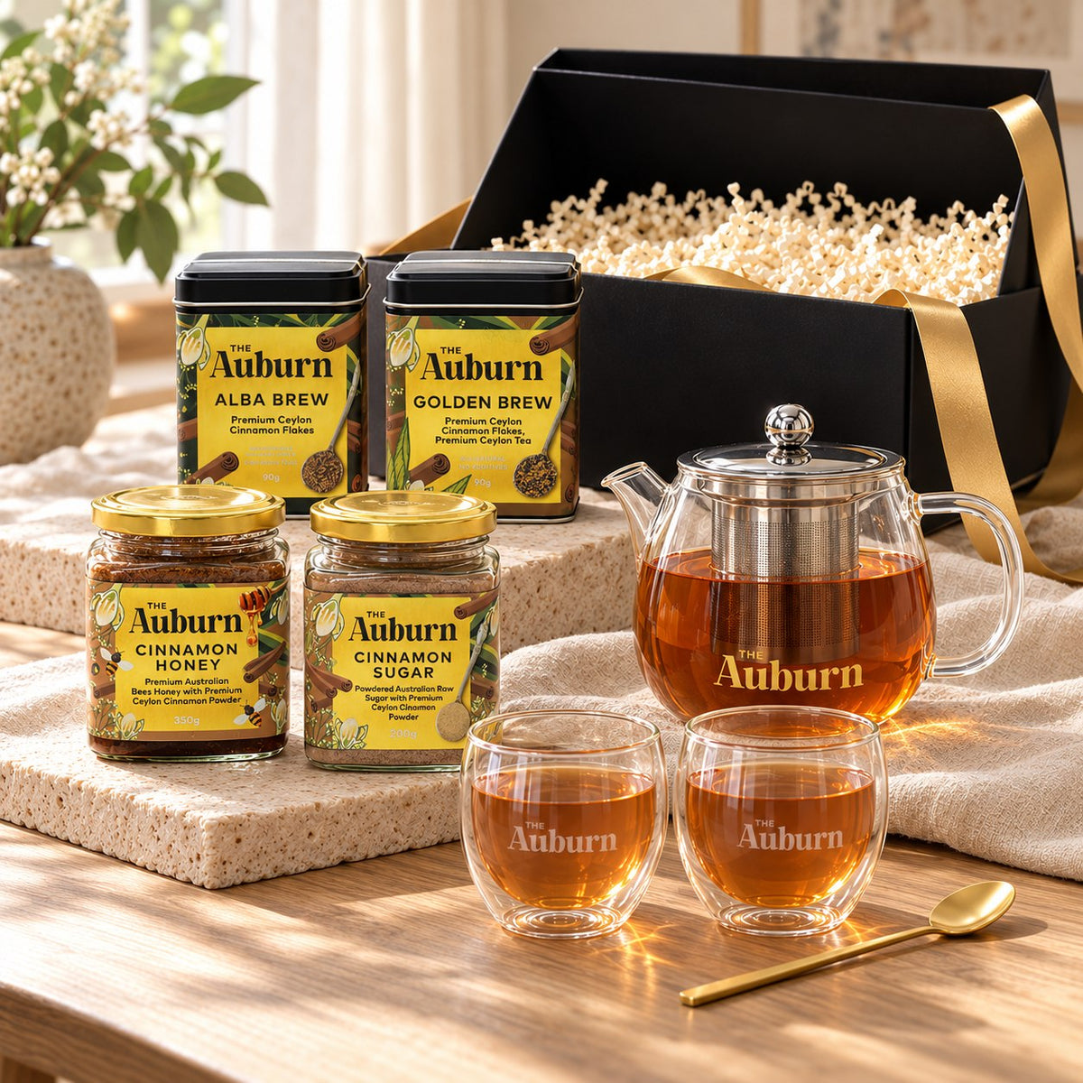 The Big Celebration hamper: Alba and Golden Brew tins, a glass teapot, two glass mugs, jars of cinnamon honey and sugar, and a gold tea spoon.