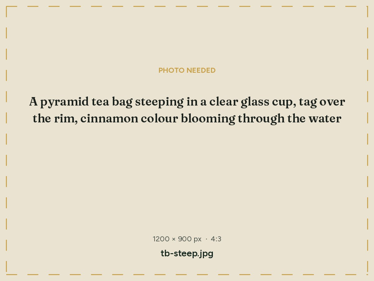An Auburn pyramid tea bag steeping in a clear glass cup
