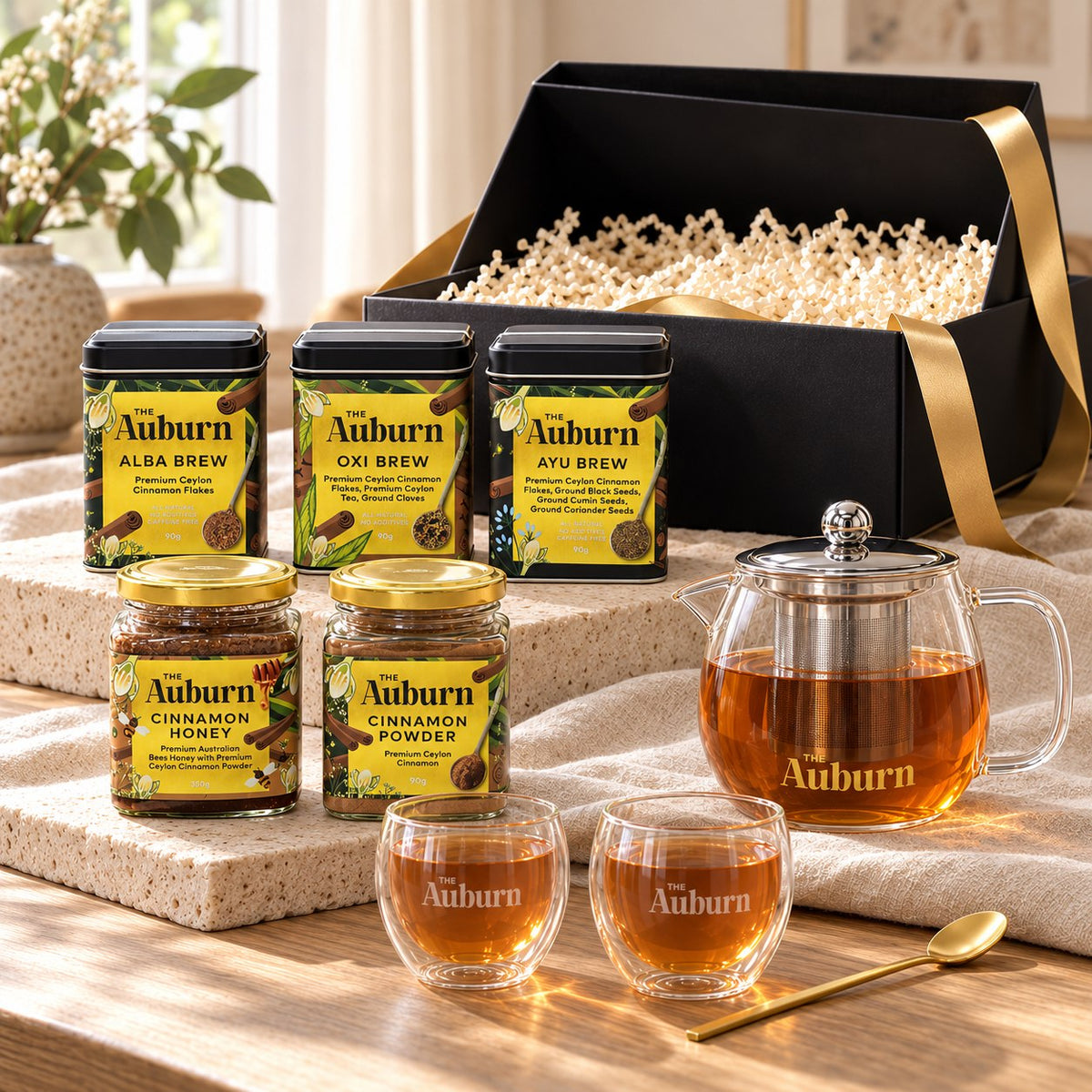 Feeling GRATEFUL hamper: Alba, Oxi and Ayu Brew tins, a glass teapot, two glass mugs, jars of cinnamon honey and powder, and a gold tea spoon.